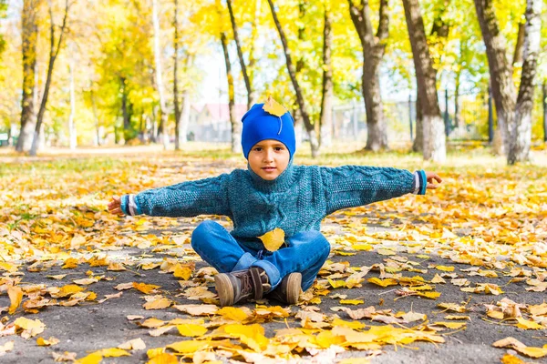 Мальчик бросает осенние листья в парке — стоковое фото