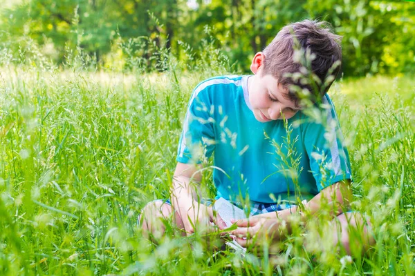Chico leyendo un libro sentado en la hierba — Foto de Stock