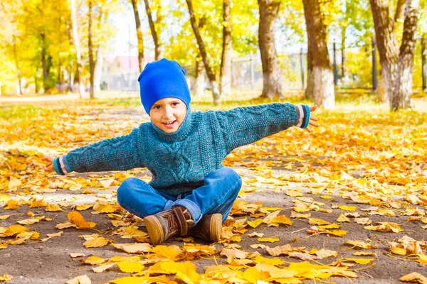 Улыбающийся мальчик в шляпе и свитере, сидящий в парке на ауту — стоковое фото