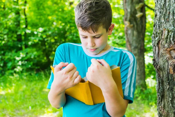 Мальчик-подросток стоит с книгой у дерева летом — стоковое фото
