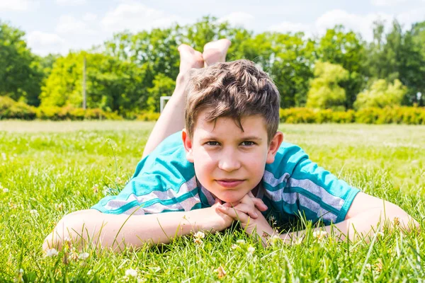 Smiling boy lying on the grass on his stomach — Stock Photo, Image