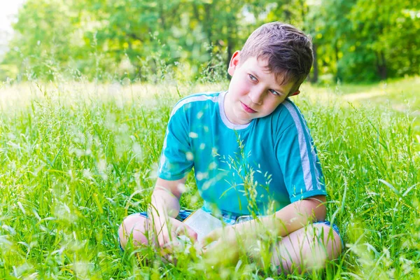 Boy reading a book sitting on the grass — Stock Photo, Image