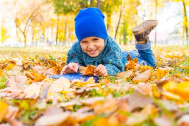 bir kitap ile sarı yaprakları üzerinde yatan neşeli çocuk