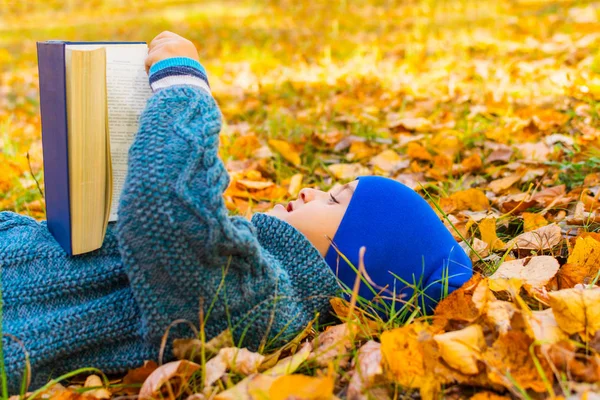 Boy is reading a book lying on the leaves in autumn — Stock Photo, Image