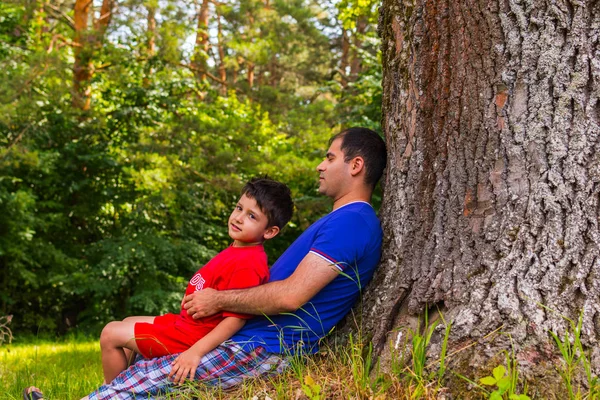 Отец и сын отдыхают под деревом летом — стоковое фото