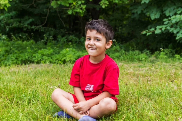 Веселый мальчик, сидящий на траве летом — стоковое фото