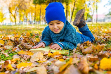 bir kitap ile sarı yaprakları üzerinde yatan neşeli çocuk