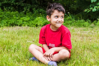 Yaz aylarında çim üzerinde oturan neşeli çocuk