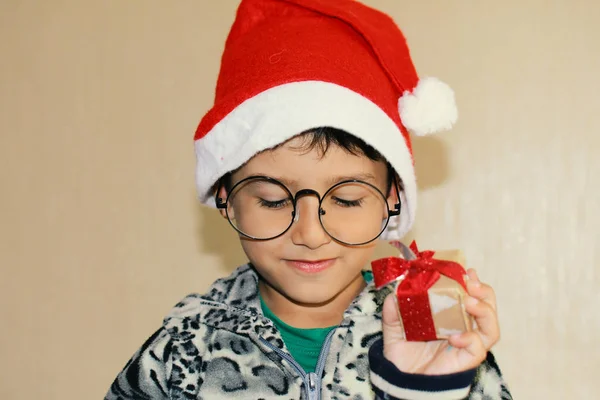 Niño con gafas y sombrero de Santa sosteniendo un pequeño regalo —  Fotos de Stock