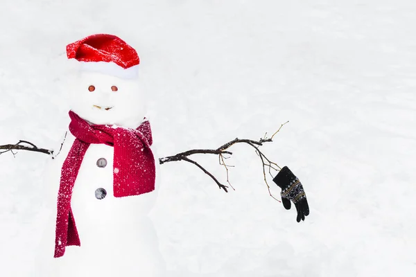 Legrační sněhulák v šále Santa a klobouk na zasněženém pozadí — Stock fotografie