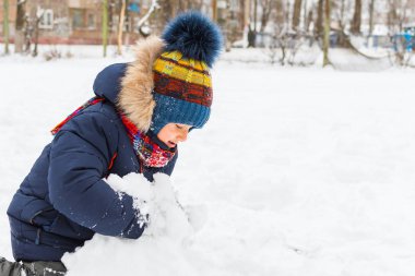 Çocuk 5 yaşında, kışın dışarıda karla oynuyor.