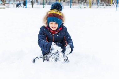 Çocuk 5 yaşında, kışın dışarıda karla oynuyor.