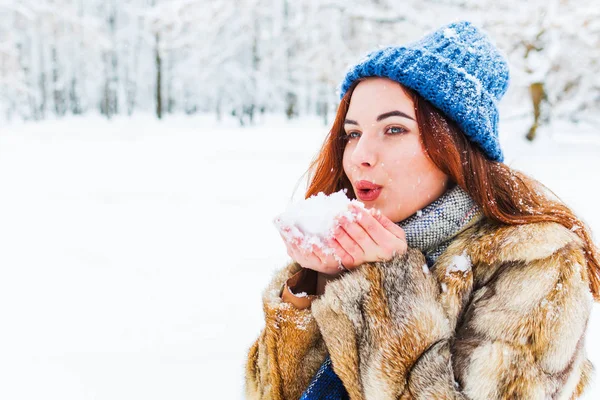 Encantadora jovem mulher em azul chapéu de malha soprando na neve — Fotografia de Stock