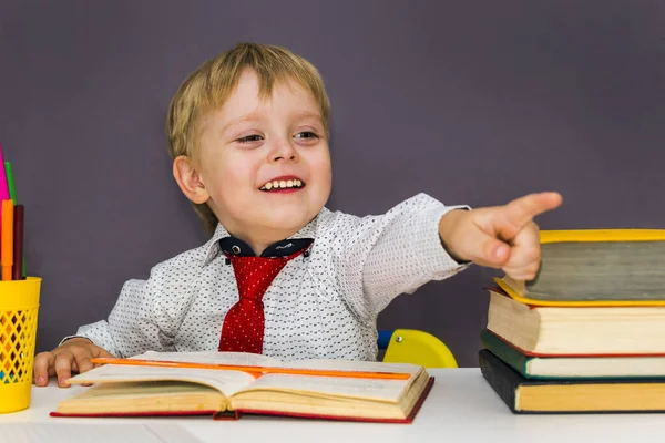 Glad Pojke Vid Ett Bord Med Böcker Pekar Med Fingret — Stockfoto