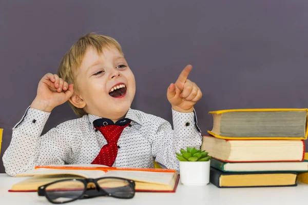 Glad Pojke Vid Ett Bord Med Böcker Pekar Med Fingret — Stockfoto