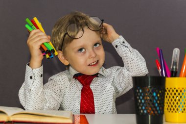 Elinde keçeli kalemlerle anaokulu çocuğu. Masada sarışın bir çocuk oturuyor..