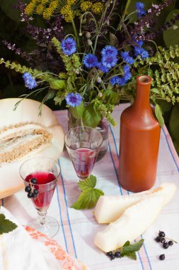 Beyaz masa örtüsü üzerinde kavun ve cornflowers buketi ile natürmort