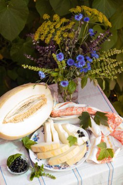 Beyaz masa örtüsü üzerinde kavun ve cornflowers buketi ile natürmort