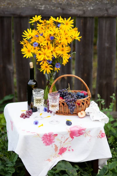 Boeket van bloemen, wijn, glazen en druiven tegen de achtergrond van een oud hek — Stockfoto