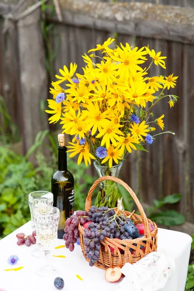 Boeket van bloemen, wijn, glazen en druiven tegen de achtergrond van een oud hek — Stockfoto