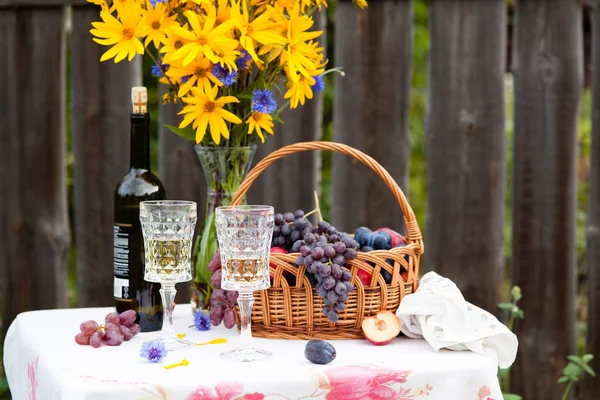 Boeket van bloemen, wijn, glazen en druiven tegen de achtergrond van een oud hek — Stockfoto