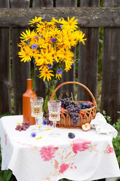 Boeket van bloemen, wijn, glazen en druiven tegen de achtergrond van een oud hek — Stockfoto