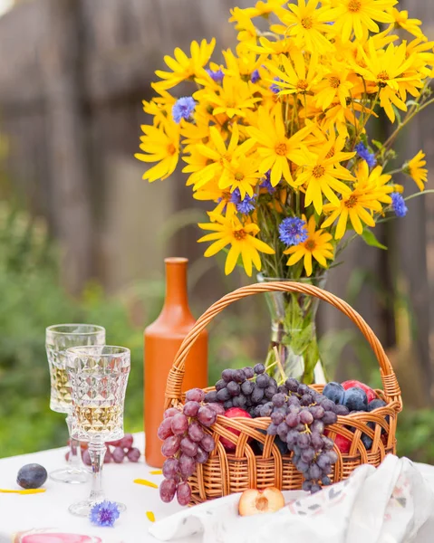 Boeket van bloemen, wijn, glazen en druiven tegen de achtergrond van een oud hek — Stockfoto