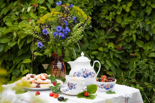 Martwa żywotność z bukietem kwiatów, herbatą, ciasteczkami i jagodami na stole w ogrodzie — Zdjęcie stockowe
