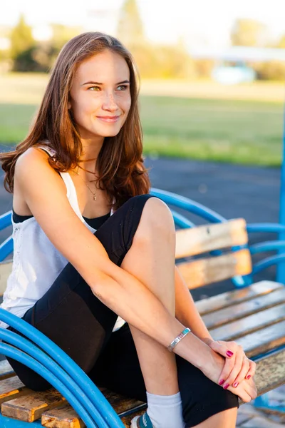 Menina bonita senta-se no banco no parque de verão — Fotografia de Stock