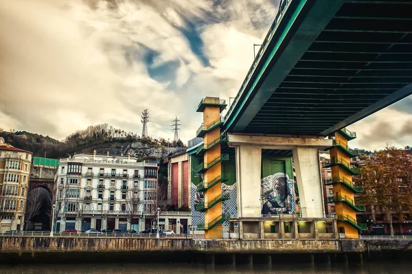 Bilbao, İspanya. Nervion Nehri üzerindeki köprülerden birinin altında şehrin manzarası ve grafiti. 