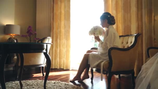 Junge Braut sitzt mit einem Blumenstrauß am Fenster eines Luxushotels — Stockvideo
