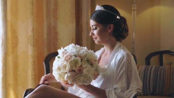 Jovem noiva está sentada à janela em um hotel de luxo com um buquê de flores — Vídeo de Stock