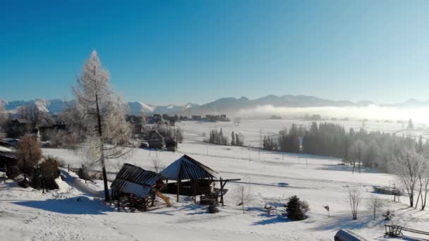 Вид с воздуха на старые деревянные здания на снежной местности в горах с ярко-голубым небом — стоковое видео