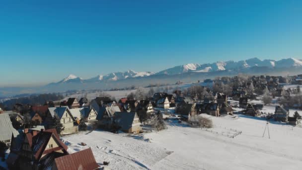Vue par drone de chalets et maisons sur terrain enneigé dans les montagnes avec un soleil éclatant — Video