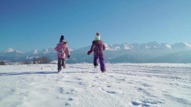 Güneş arka planda güzel dağlar ile karlı arazi üzerinde çalışan giyim Charming çocuklar