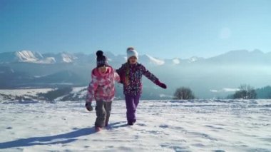 Güneş arka planda güzel dağlar ile karlı arazi üzerinde çalışan giyim Charming çocuklar