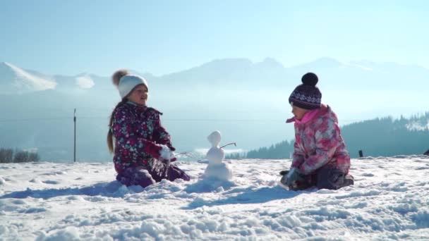 Glada små flickor i ytterkläder ha roligt och kasta snö i solljus står utomhus — Stockvideo