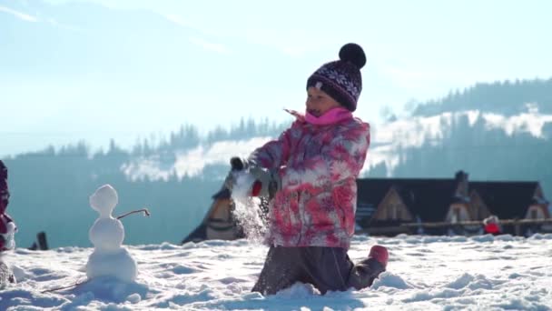 Alegre niñas en outwear divertirse y tirar nieve en la luz del sol de pie al aire libre — Vídeos de Stock