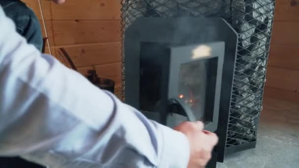 Чоловік розпалює піч у сауні, дерев'яна піч у сауні . — стокове відео
