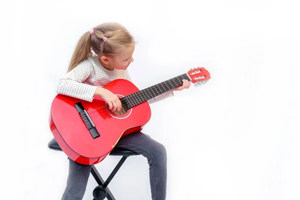 litle sarışın kız oturur ve kırmızı gitar çalar