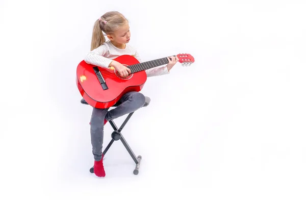 Litle blond meisje zit en speelt de rode gitaar Rechtenvrije Stockafbeeldingen