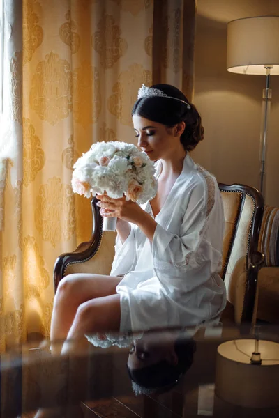 Hermosa novia está sentada junto a la ventana con flores en un hotel de lujo — Foto de Stock