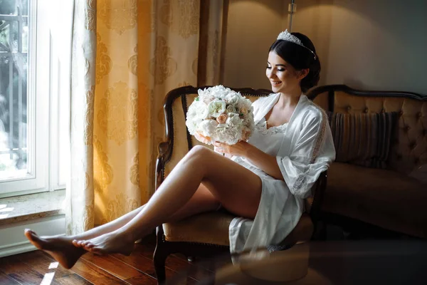 beautiful bride is sitting by the window with flowers in a luxury hotel