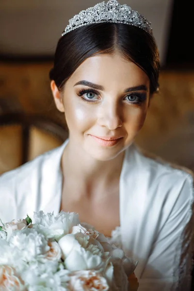 Beautiful bride is sitting by the window with flowers in a luxury hotel — Stock Photo, Image