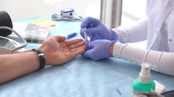 Closeup anonieme arts in latex handschoenen piercing vinger en het nemen van bloedmonster van de patiënt tijdens het werken in het moderne ziekenhuis Stockfoto