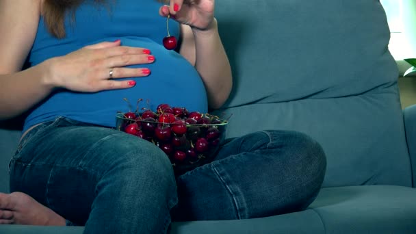 Беременная мать ласкает огромный животик и ест вишневые ягоды — стоковое видео
