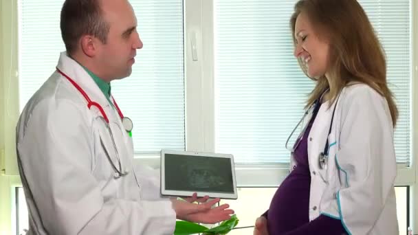 Врач мужчина и беременная коллега показывают ультразвуковое фото в планшетном компьютере — стоковое видео