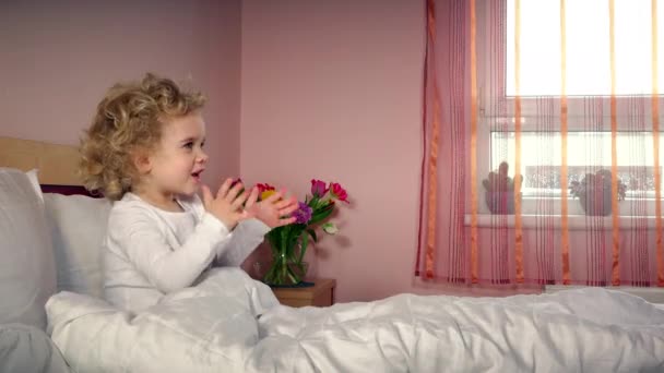 Pequena menina alegre palmas mãos e obter caixa de presente na cama — Vídeo de Stock