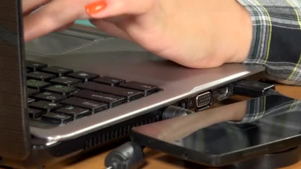 Mãos de mulher usando computador portátil e carga de telefone no carregador sem fio. Fechar. — Vídeo de Stock