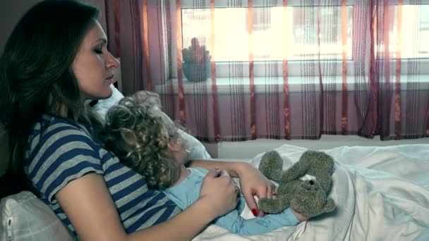 Biedny chory dziecko dziewczynka z miś pluszowy przyjaciel i matka siedzi razem w łóżku — Wideo stockowe